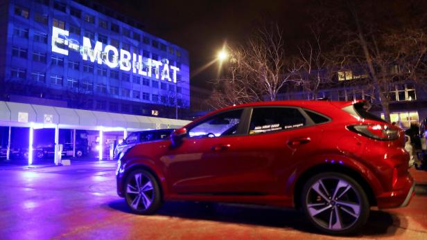 Elektroauto vor einem Gebäude mit darauf projiziertem E-Mobilität Schriftzug.