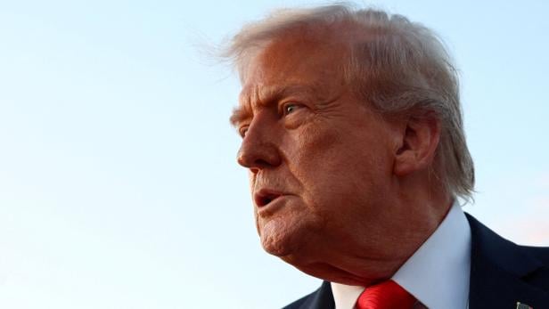 U.S. President Donald Trump speaks to the press at Joint Base Andrews Donald Trump mit roter Krawatte blickt zur Seite, am Revers ist eine kleine US-Flagge.