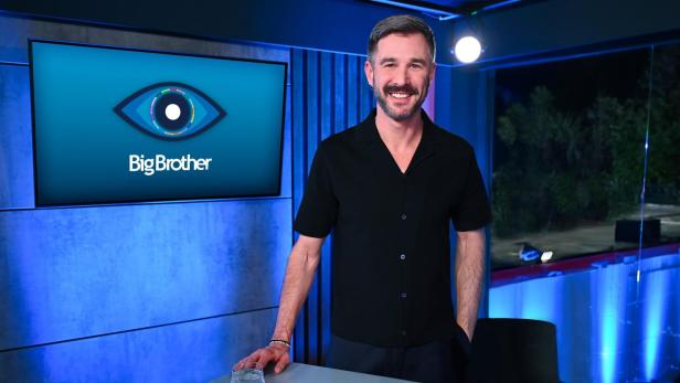 Jochen Schropp steht lächelnd vor einem Bildschirm mit dem "Big Brother"-Logo in einem blau beleuchteten Studio. Jochen Schropp steht lächelnd vor einem Bildschirm mit dem "Big Brother"-Logo in einem blau beleuchteten Studio.
