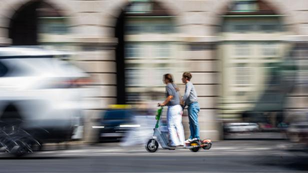 Zwei Menschen fahren auf einem E-Scooter.
