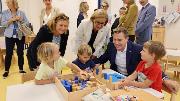 Gruppe Erwachsener beugt sich über Tisch mit Kindern in Kindergarten