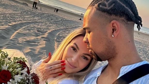 Anita Latifi posiert mit ihrem Partner und einem Blumenstrauß verliebt am Strand