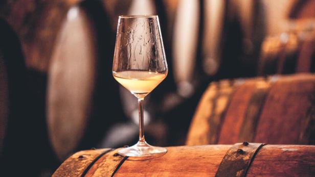 Ein Glas Weißwein steht auf einem Holzfass im Weinkeller.