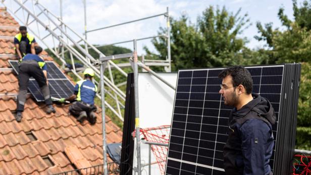 Arbeiter installieren eine PV-Anlage auf dem Dach eines Einfamilienhauses.