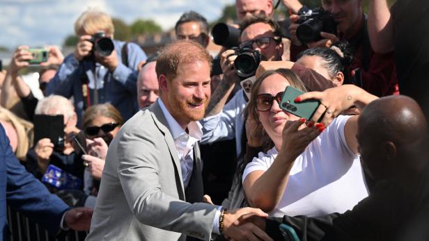 Prinz Harry Prinz Harry schüttelt Hände, während umstehende Menschen Fotos mit Kameras und Handys machen.