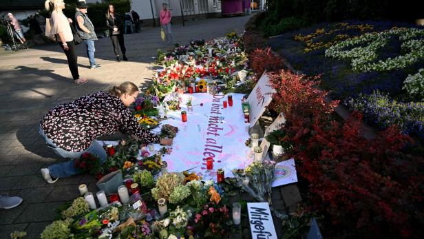FILES-GERMANY-CRIME-GOVERNMENT-EXTREMISM Eine Frau legt Blumen an einer Gedenkstätte mit Kerzen, Blumen und Botschaften nieder, während andere Menschen respektvoll stehen.