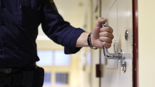 THEMENBILD-PAKET: JUSTIZANSTALT / STRAFVOLLZUG / MASSNAHMENVOLLZUG Eine Person in Uniform öffnet mit der rechten Hand eine schwere Tür mit Metallgriff in einem Flur.