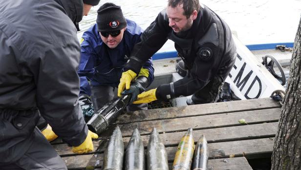 Drei Männer heben Munition aus Boot auf Steg