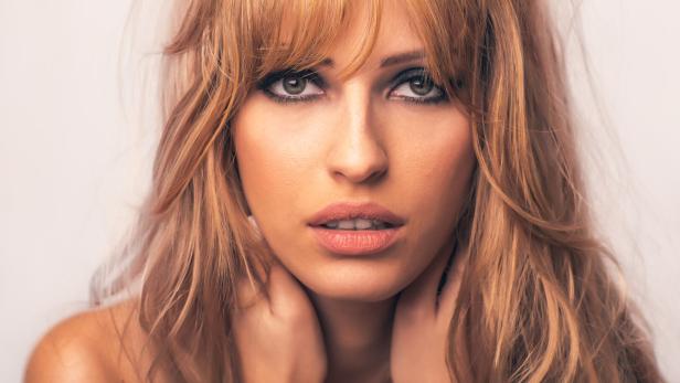 Eine Frau mit rotblondem langen Haar sieht in Großaufnahme in die Kamera.