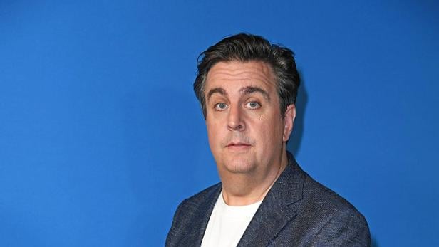 Bastian Pastewka Bastian Pastewka steht im Anzug vor blauem Hintergrund.