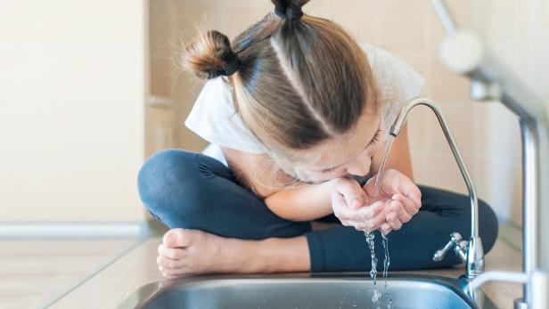 Mädchen trinkt Wasser aus dem Wasserhahn