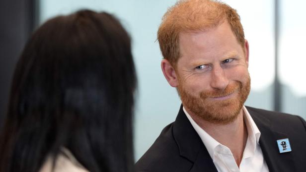 Prinz Harry blickt mit einem Lächeln auf eine Person mit dunklen Haaren.