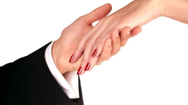 Frauenhand mit roten Fingernägeln liegt in elegante Männerhand.