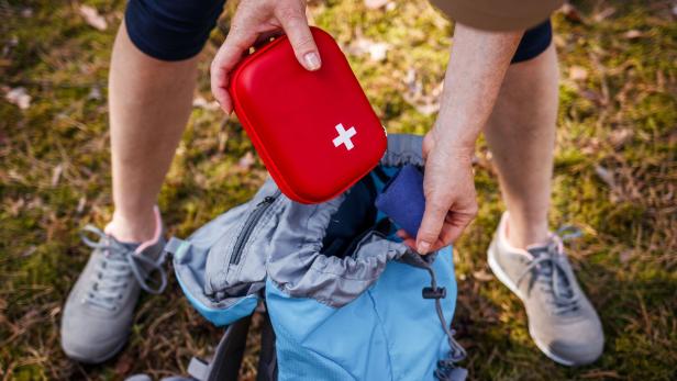 Eine Person packt eine rote Erste-Hilfe-Tasche in einen blauen Rucksack.
