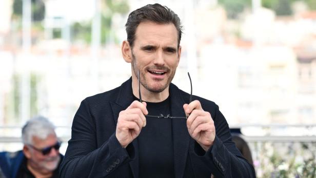 Matt Dillon hält seine Brille in den Händen und lächelt.