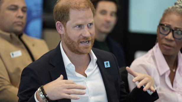 Prinz Harry spricht gestikulierend in einer Gesprächsrunde, umgeben von aufmerksam zuhörenden Personen.