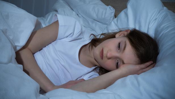 Das Bild zeigt eine junge Frau mit Schlafproblemen wach im Bett. 