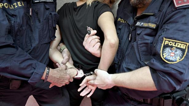Zwei Beamte legen einer Frau vorschriftmäßig Handschellen an.