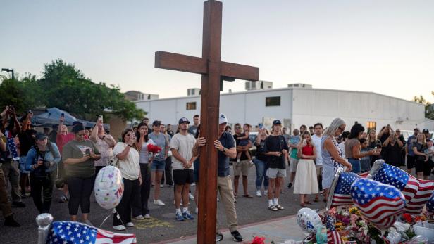 Menschen versammeln sich um ein großes Holzkreuz und legen Blumen sowie US-Flaggen als Zeichen der Trauer nieder.