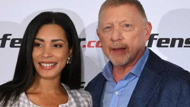 Boris Becker posiert mit seiner Frau Lilian vor einer Wand mit Logos.