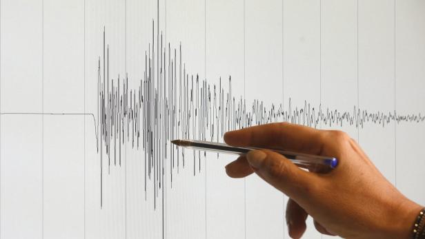 Eine Hand deutet mit einem Stift auf eine seismografische Aufzeichnung.