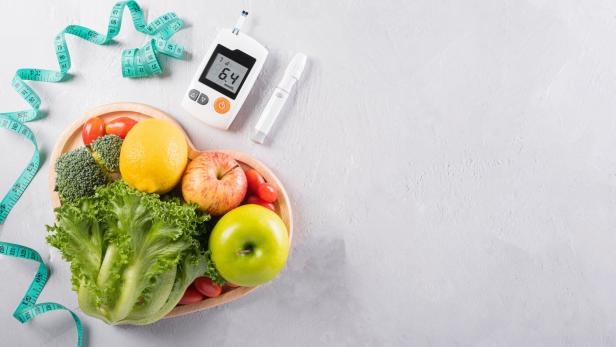 Gemüse, Obst und ein Insulinmessgerät liegen auf einem Tisch.