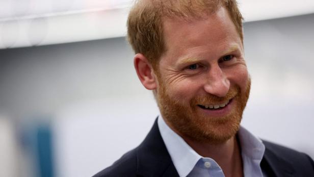 Ein lächelnder Prinz Harry ist in einem dunklen Sakko und hellblauem Hemd zu sehen.