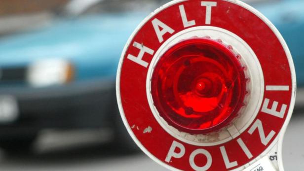 Eine rote Polizeikelle mit der Aufschrift „Halt Polizei“ wird vor einem unscharfen Auto gezeigt.
