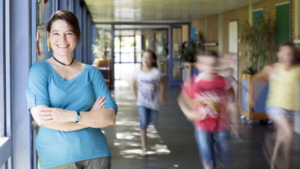 portrait of female teacher, leaning at corridor wall, running children in background portrait of female teacher, leaning at corridor wall, running children in background