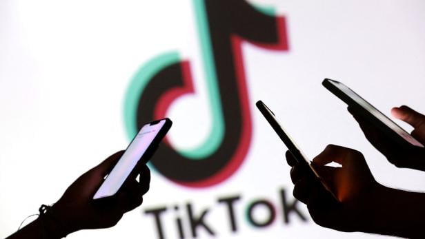 Illustration shows teenagers pose for a photo while holding smartphones in front of a TikTok logo