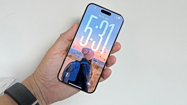 Eine Hand hält ein iPhone mit dem Sperrbildschirm, der eine Frau mit Rucksack in Kappadokien zeigt.