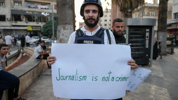 Ein syrischer Journalist hält ein Plakat mit der Aufschrift „Journalismus ist kein Verbrechen“ hoch.