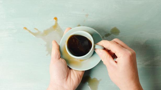 Hände umschließen eine Tasse Kaffee, wobei etwas Kaffee verschüttet ist.