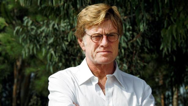 Robert Redford Robert Redford mit verschränkten Armen und weißem Hemd vor Bäumen.