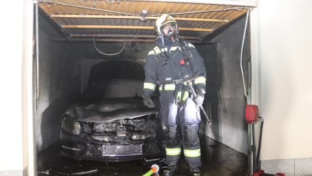 Feuerwehrmann vor ausgebranntem Auto