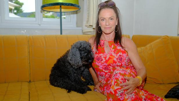 Christine Neubauer sitzt mit ihrem Hund auf einer gelben Couch