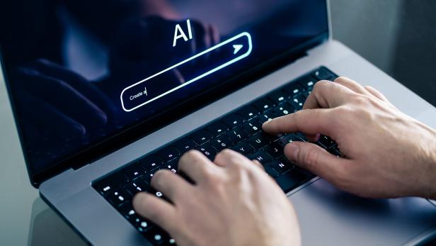 Hände tippen auf einer Laptop-Tastatur, auf dem Bildschirm steht „AI“ mit einer Suchleiste.