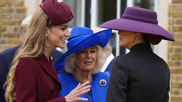 Prinzessin Kate, Königin Camilla und Melania Trump sind elegant gekleidet mit auffälligen Hüten und unterhalten sich im Freien.