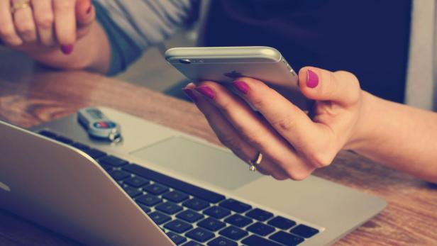 Frau hält Handy über Laptop
