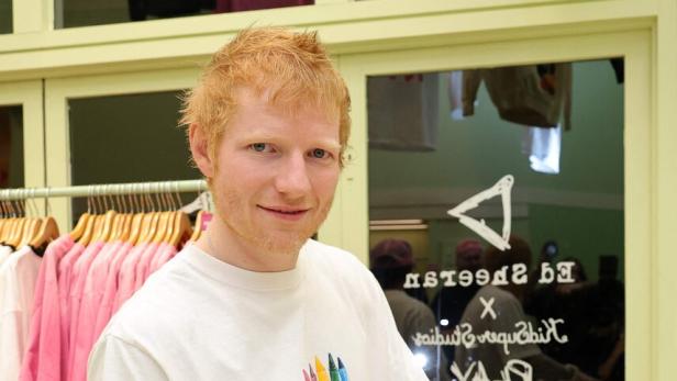 Ed Sheeran signiert einen Fußball in einem Geschäft mit Kleidung.