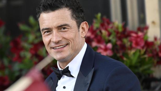 Orlando Bloom lächelt in einem dunklen Anzug mit Fliege.