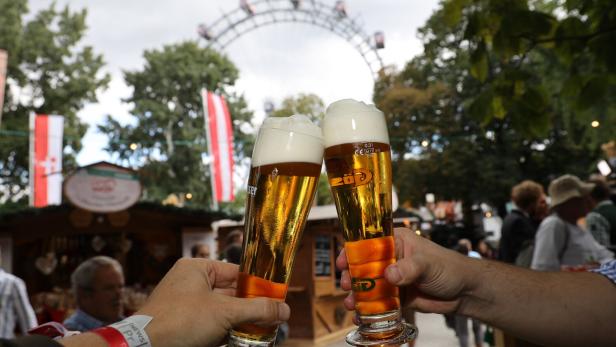 Zwei Hände mit Biergläsern, die gerade zusammenstoßen, im Hintergrund sieht man das Wiener Riesenrad.