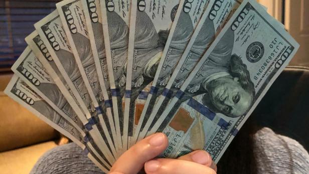 Geld gefunden: Wie ein Finder Facebook nutzt, um den Besitzer zu finden. Frau hält mehrere Dollar-Scheine in der Hand und vor dem Kopf.