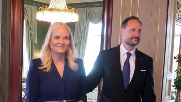 Mette-Marit und Haakon von Norwegen betreten einen Raum mit Teppich und Kronleuchter.