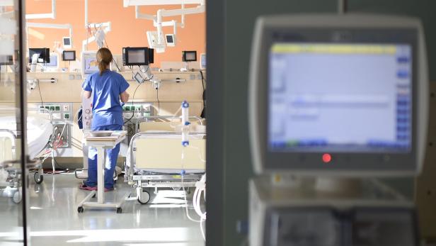 Spitalszimmer mit Monitor im Vordergrund, Betten und Pflegekraft im Hintergrund