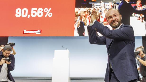Max Lercher im Anzug applaudiert lächelnd auf einer Bühne, im Hintergrund steht 90,56 % auf einer großen Leinwand.