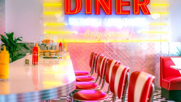 Das Interieur eines leeren Diners mit roten Barhockern und Neonreklame.