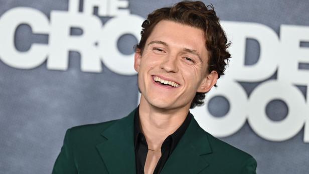 Tom Holland lächelt in einem grünen Anzug vor dem Schriftzug "The Crowded Room".