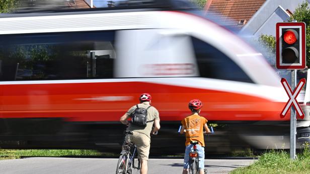 Zwei Radfahrer vor Bahnübergang mit vorbeifahrendem Zug