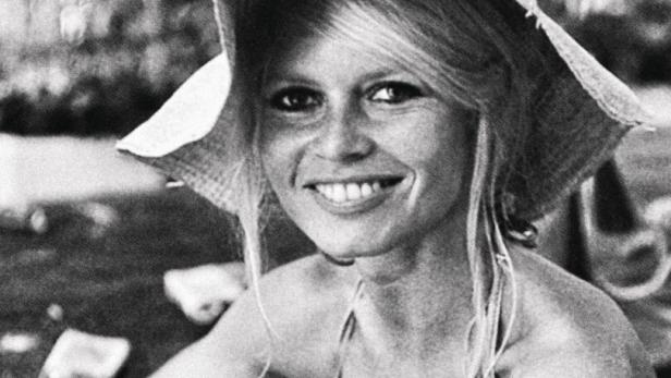Brigitte Bardot mit Hut und Gitarre lächelt.
